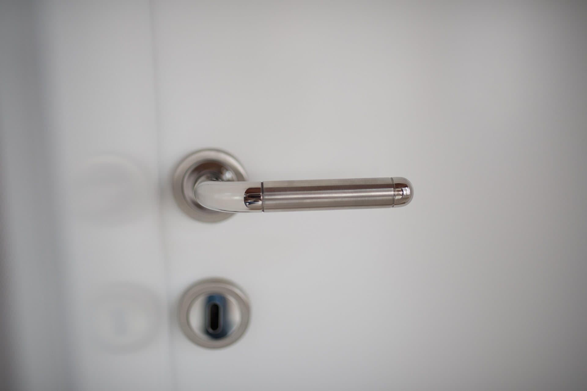 Béquille en inox brossé et entrée de cylindre sur une porte blanche, cadrage horizontal très épuré