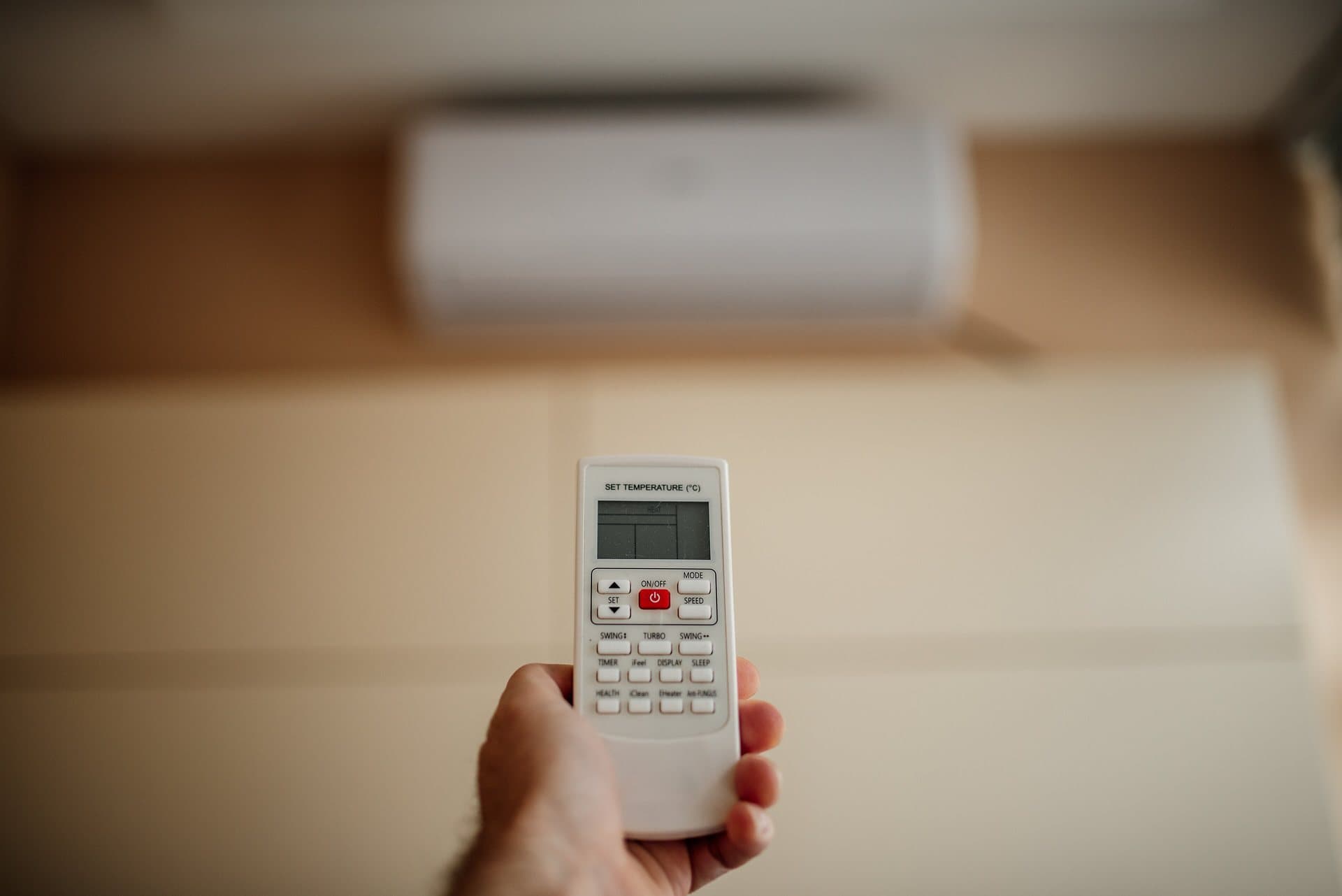 Main tenant la télécommande d'une climatisation, écran de réglage de température au premier plan et split mural blanc en arrière-plan
