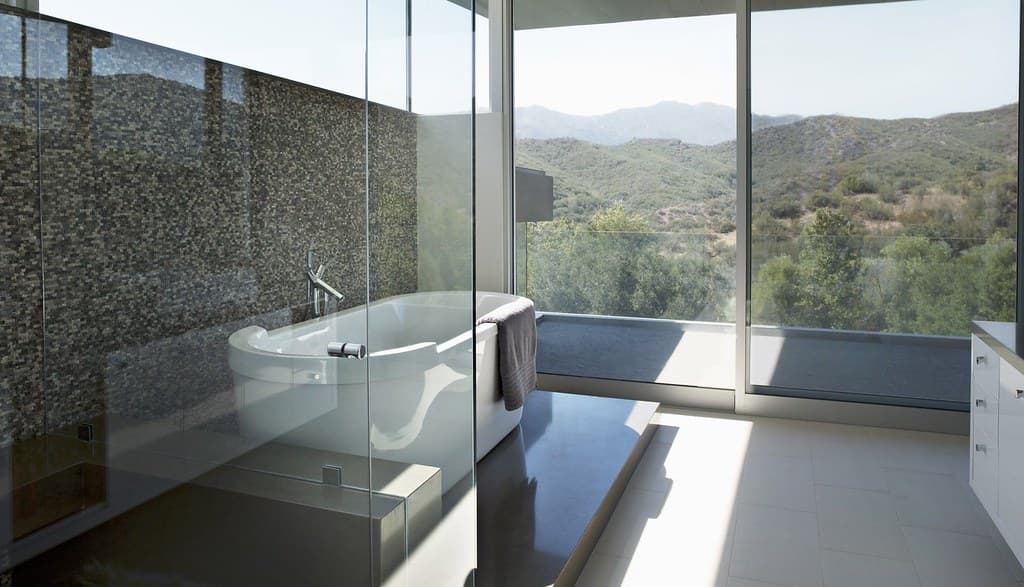 Salle de bain contemporaine avec baignoire îlot, paroi vitrée de douche et baie ouverte sur un paysage de collines